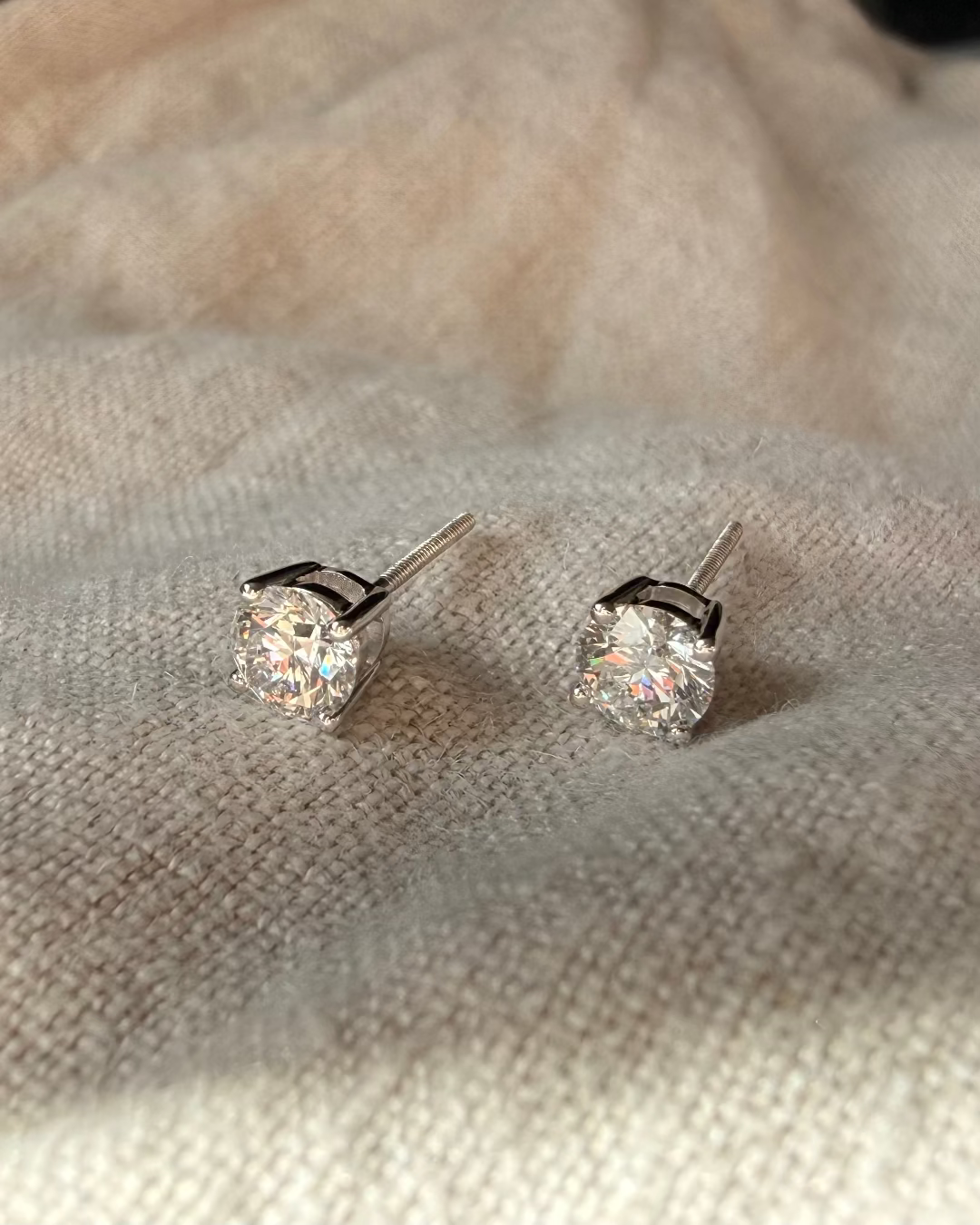 Pair of diamond stud earrings on a textured fabric background