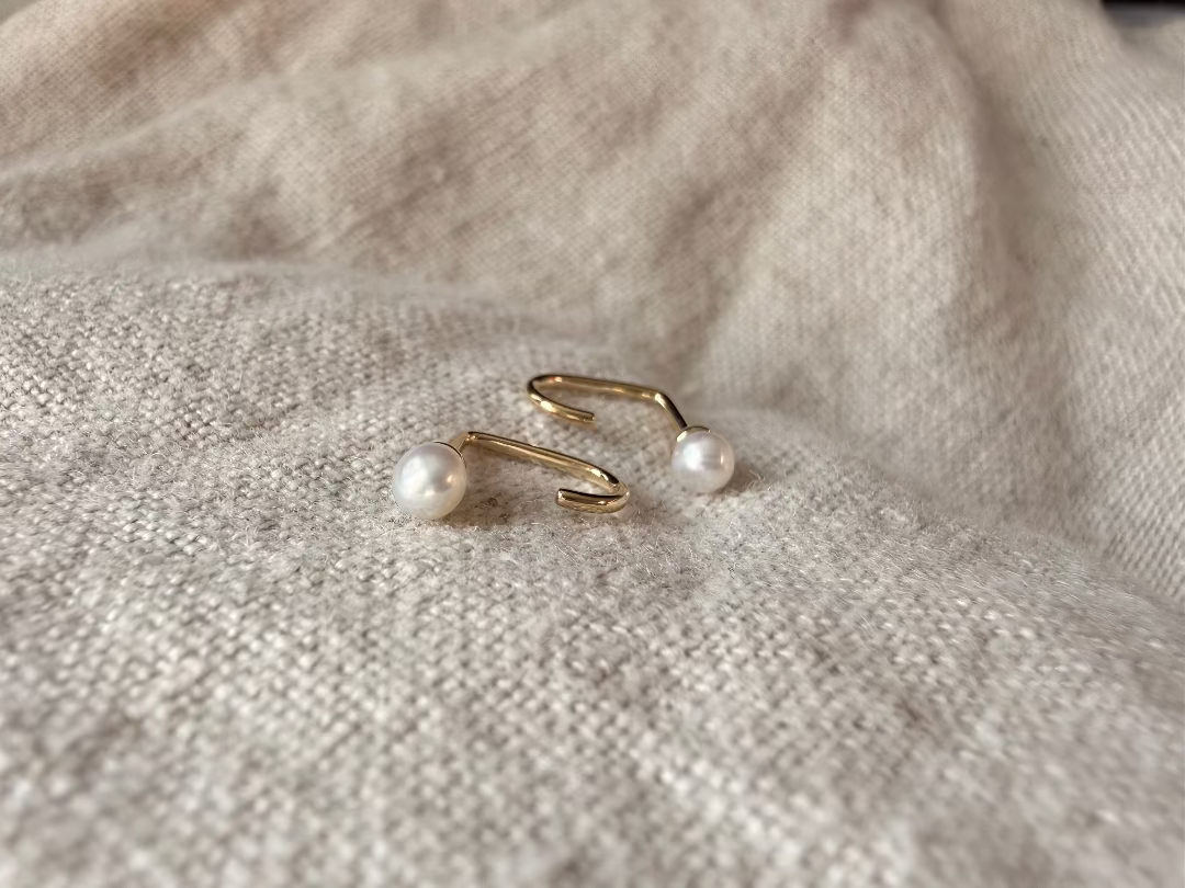 Pair of gold earrings with pearls on a textured beige fabric background