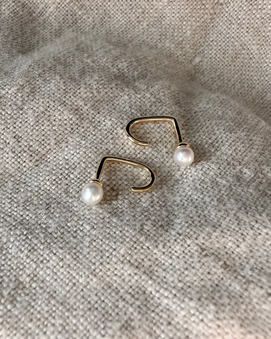 Gold nose ring with pearl beads on a textured beige background