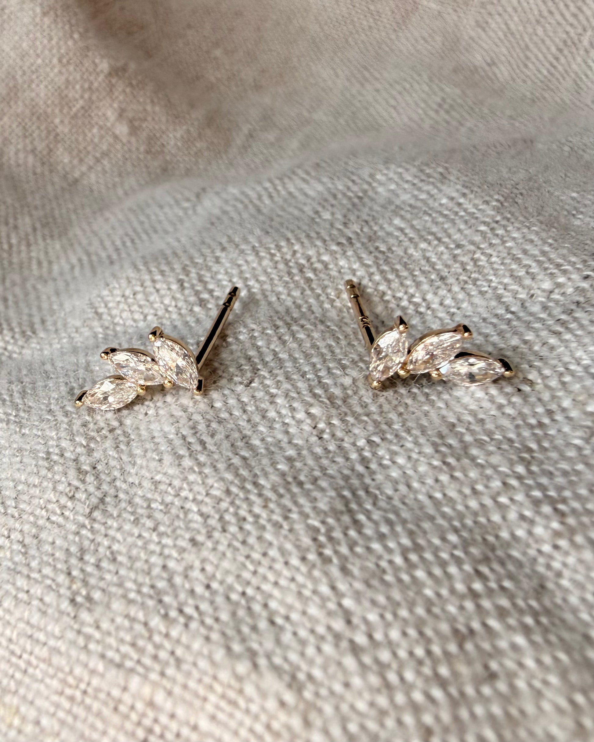 Pair of gold earrings on a textured beige fabric background