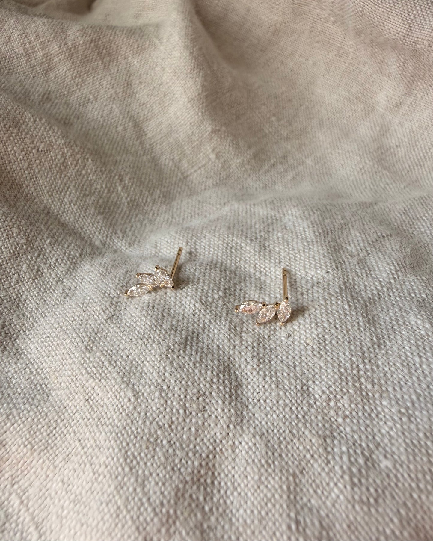 Pair of gold earrings on a textured beige fabric background
