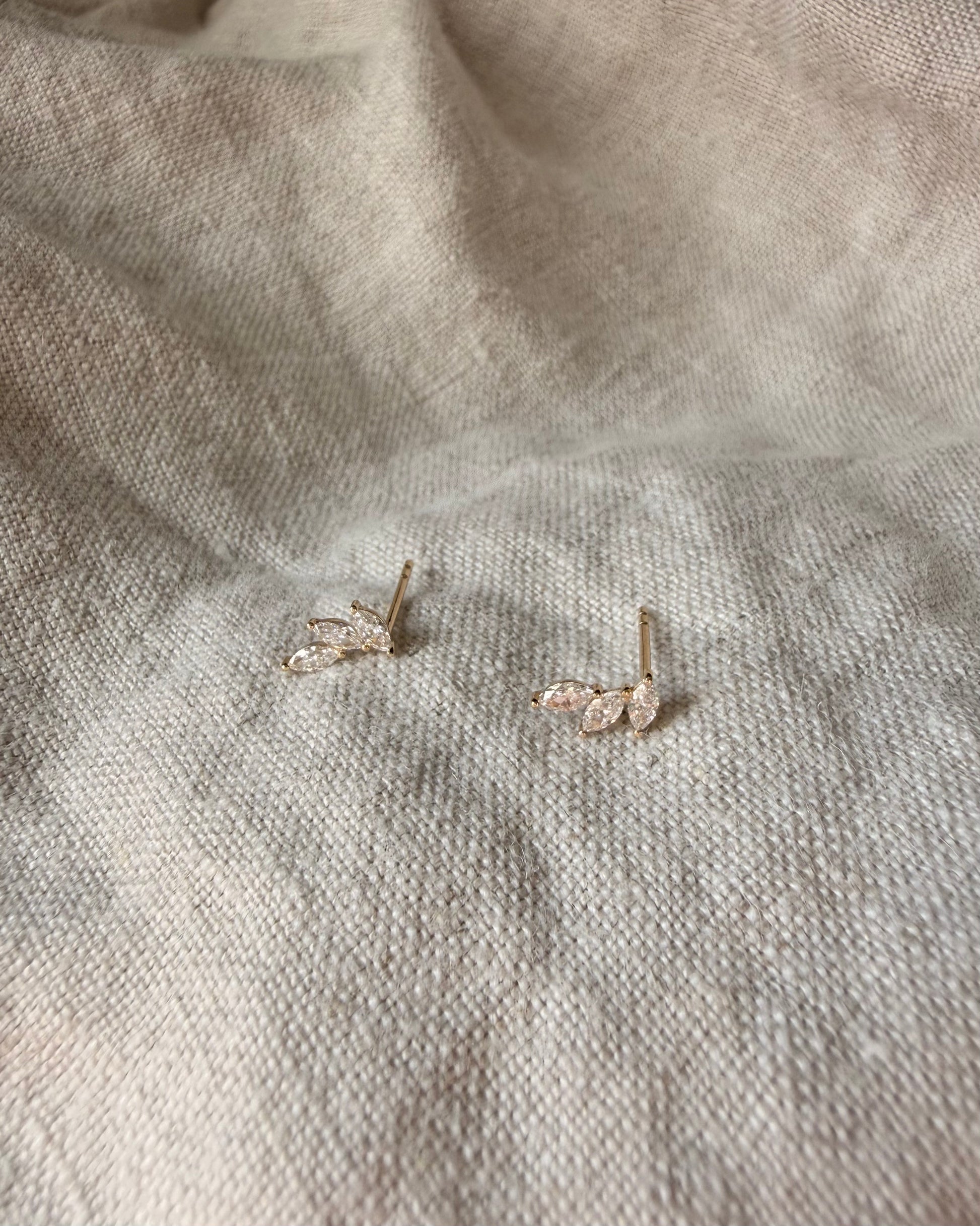 Pair of gold earrings on a textured beige fabric background